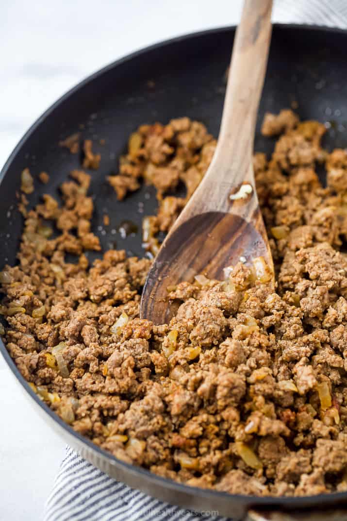 Seasoned grounded beef in a skillet with a wooden spoon stirring it