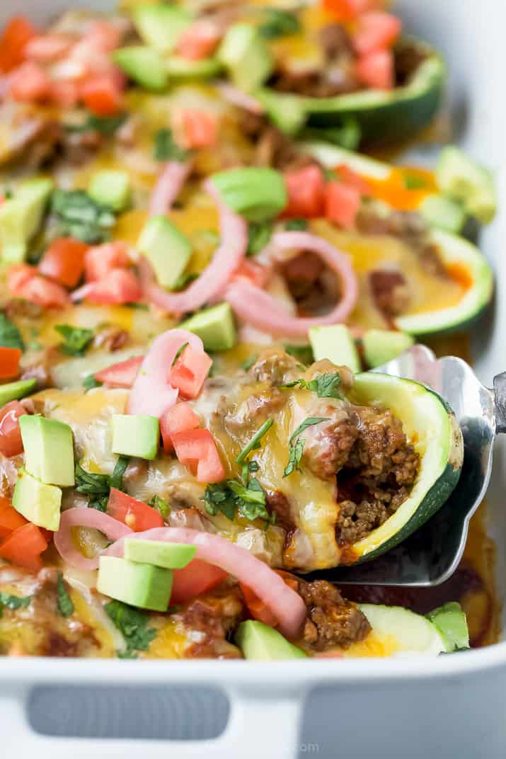 A spoon scooping a stuffed zucchini boat from a baking dish