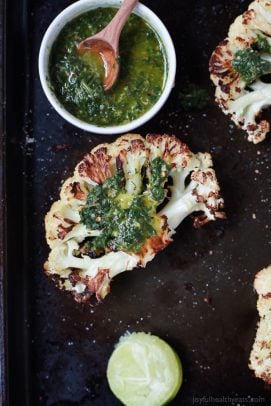 roasted cauliflower steaks with chimichurri sauce on a baking sheet