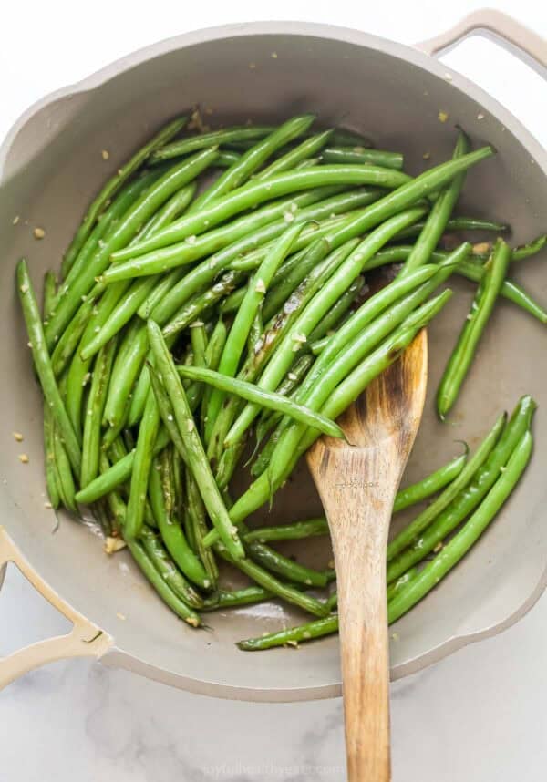 Stirring garlic green beans in skillet.