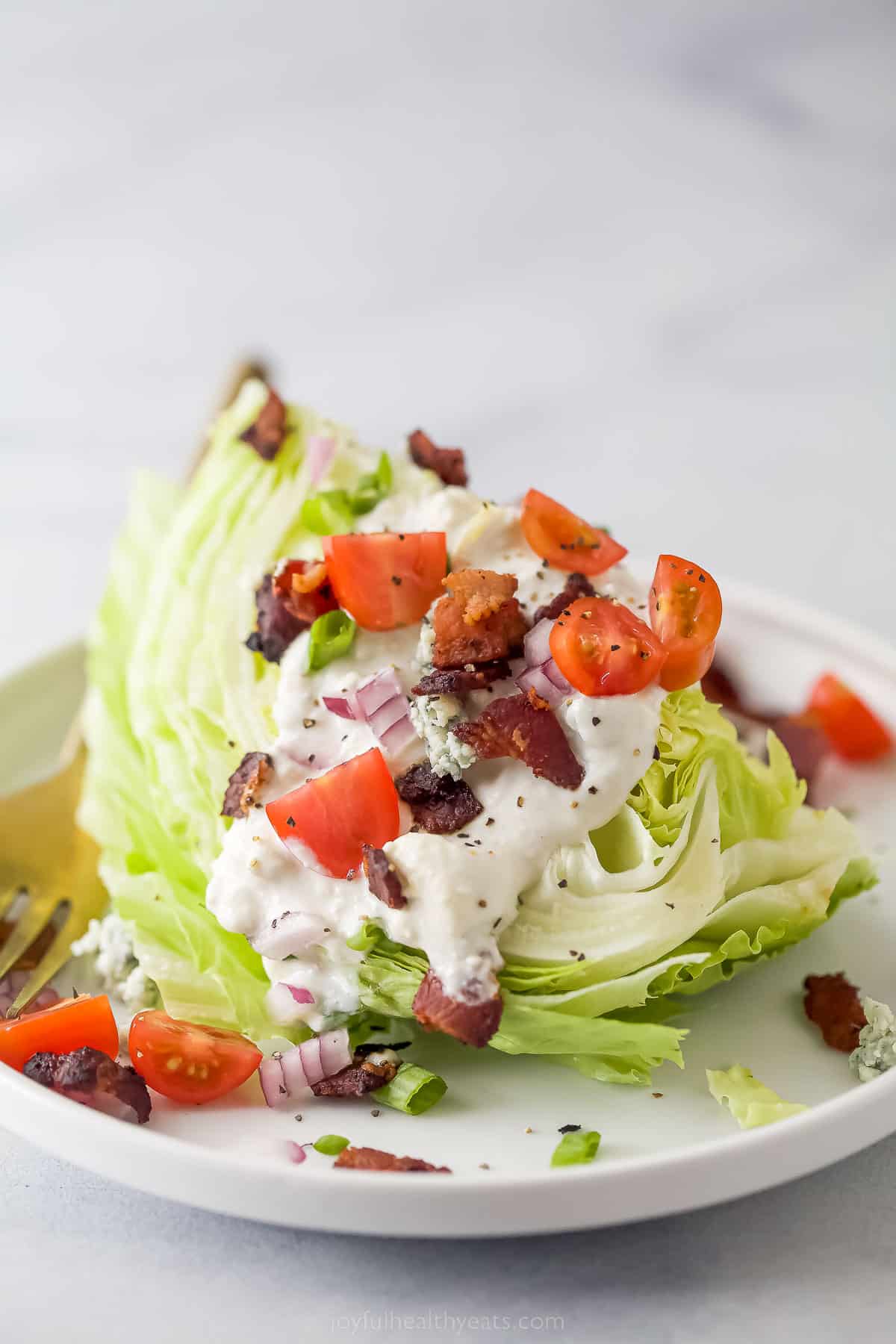 iceberg lettuce wedge with crumbled bacon, tomatoes, red onions, and blue cheese dressing