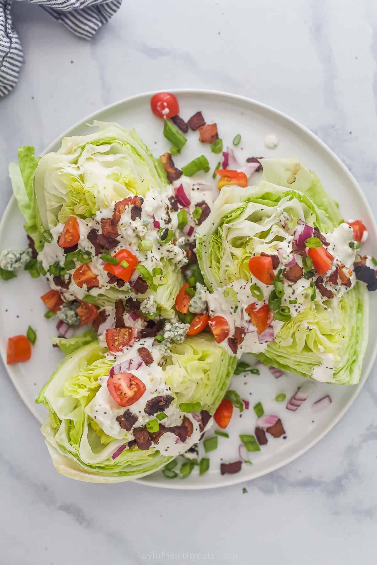 This Classic Wedge Salad with Blue Cheese Dressing is loaded with flavor from the crispy Bacon to the tangy dressing. It's light and easy! Wedge Salad with iceberg lettuce, tomatoes, bacon, red onions and creamy dressing