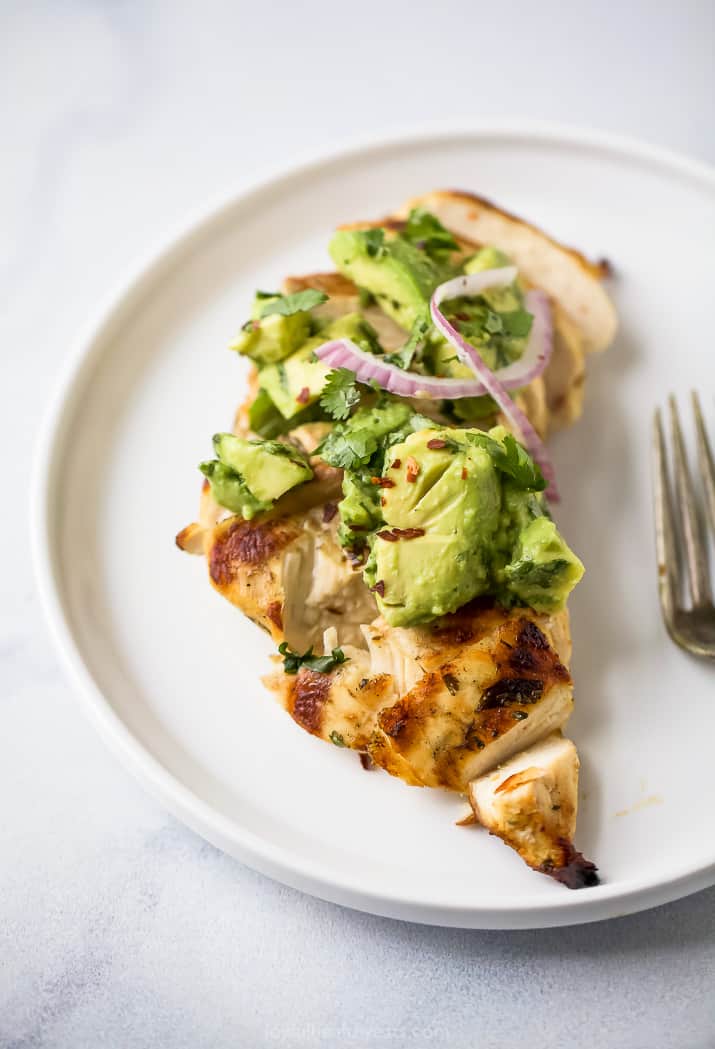 sliced cilantro lime chicken on a plate topped with avocado salsa