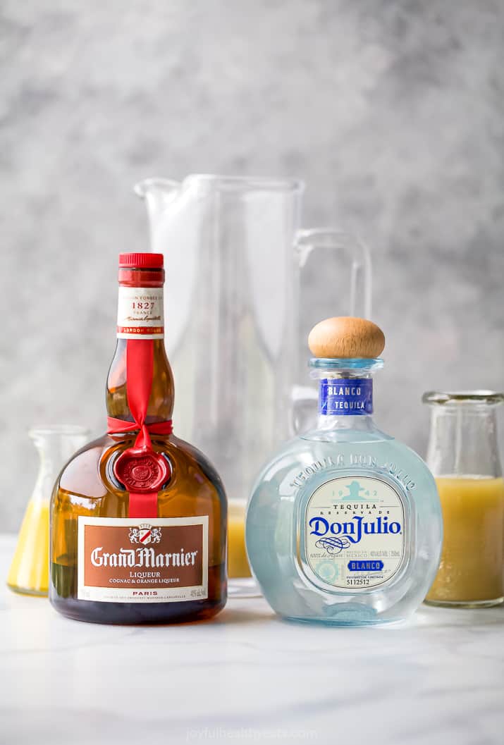 bottles of grand marnier and don julio in front of pitchers of margarita