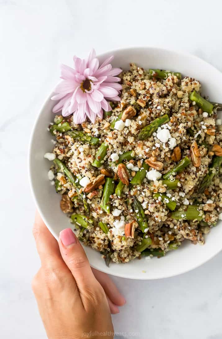 light creamy goat cheese asparagus quinoa salad in a bowl with a hand holding the bowl