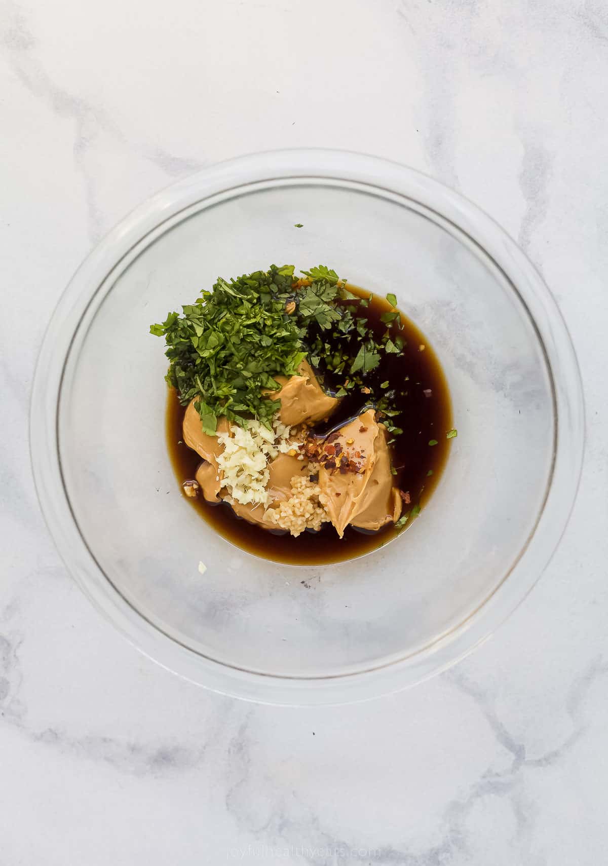 a bowl with ingredients to make peanut sauce like soy sauce, speanut butter, ginger, and herbs