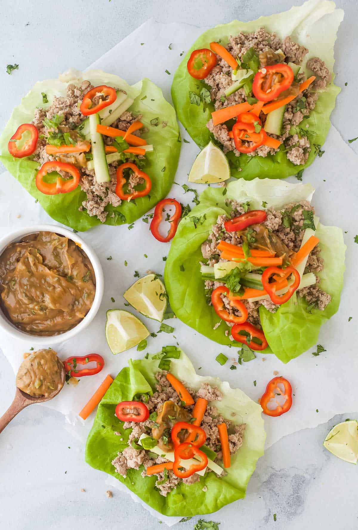 These easy Thai Chicken Lettuce Wraps are made with chicken, ginger, cilantro, fresh vegetables and slathered in a Spicy Peanut Sauce. Thai Chicken Lettuce Wraps with Spicy Peanut Sauce on a plate with a side of peanut sauce and limes