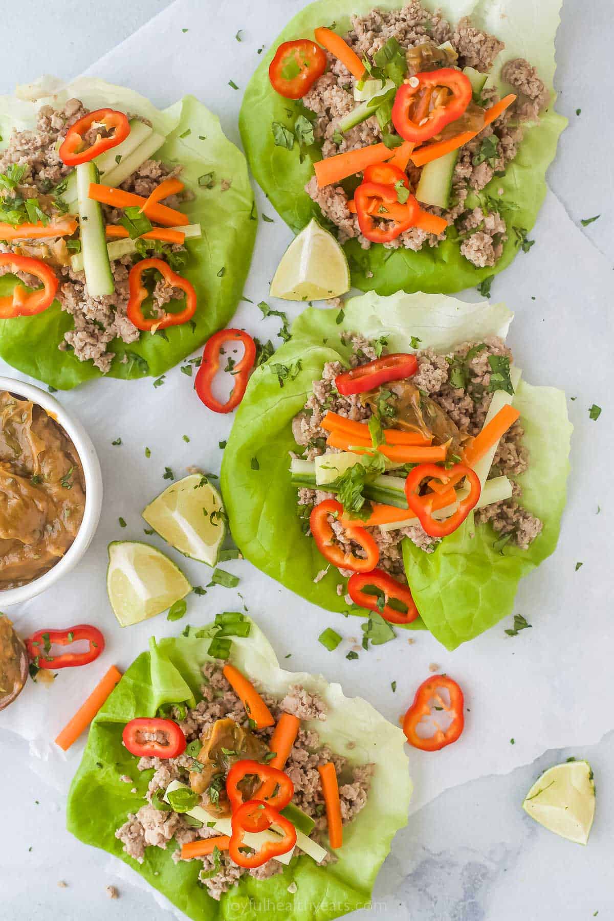 Thai Chicken Lettuce Wraps with Spicy Peanut Sauce on a plate with a side of peanut sauce and limes