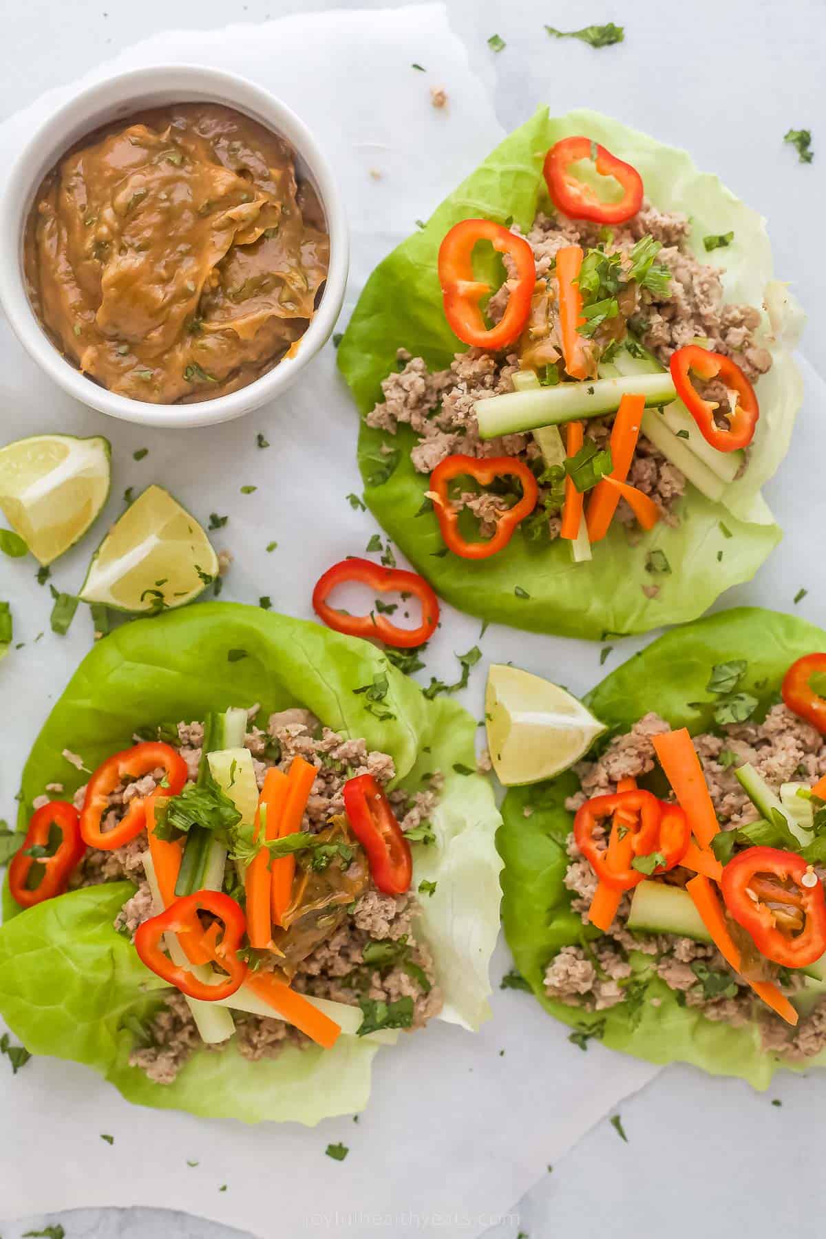 These easy Thai Chicken Lettuce Wraps are made with chicken, ginger, cilantro, fresh vegetables and slathered in a Spicy Peanut Sauce. Thai Chicken Lettuce Wraps with Spicy Peanut Sauce on a plate with a side of peanut sauce and limes