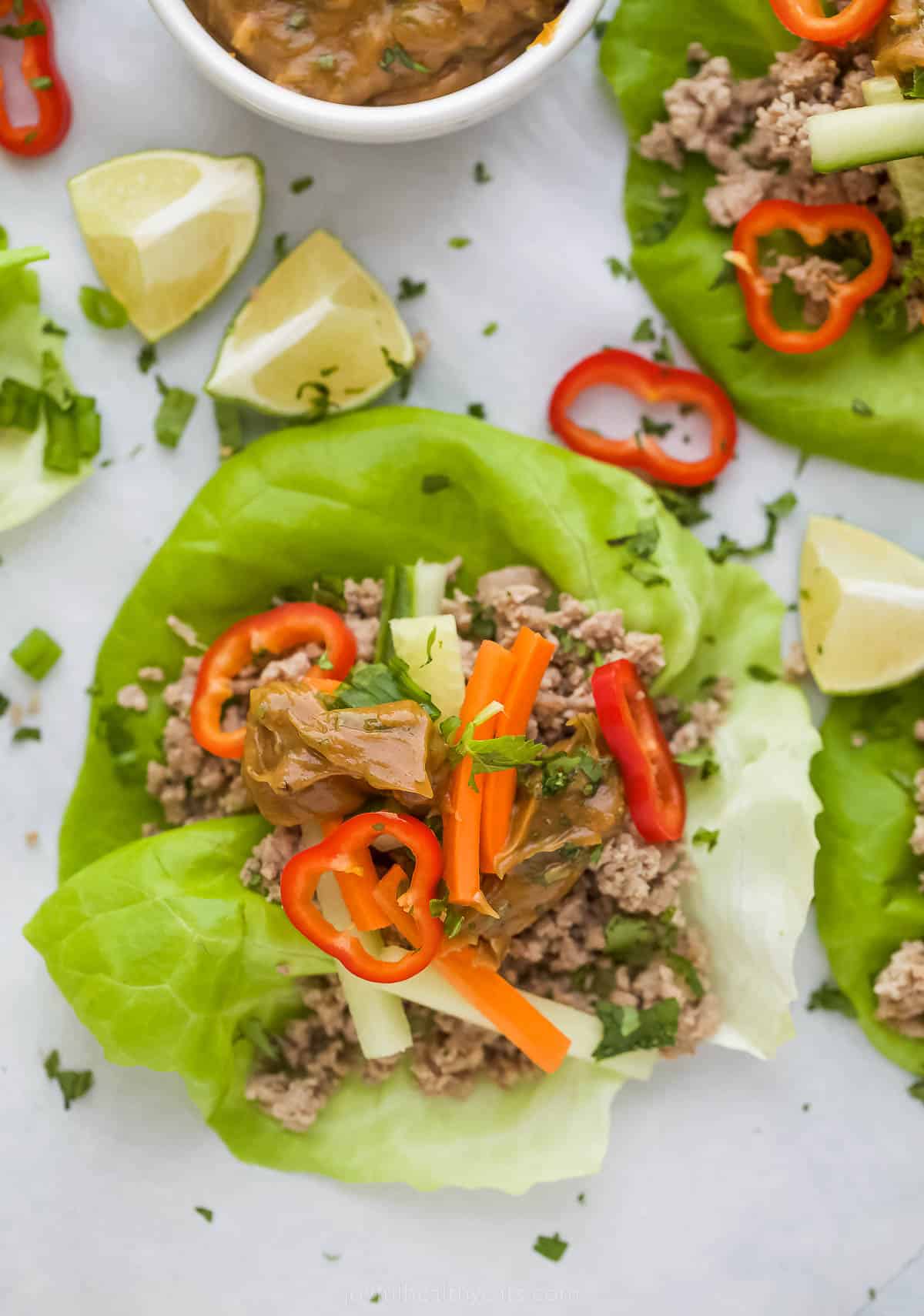 These easy Thai Chicken Lettuce Wraps are made with chicken, ginger, cilantro, fresh vegetables and slathered in a Spicy Peanut Sauce. close up on thai chicken lettuce wraps