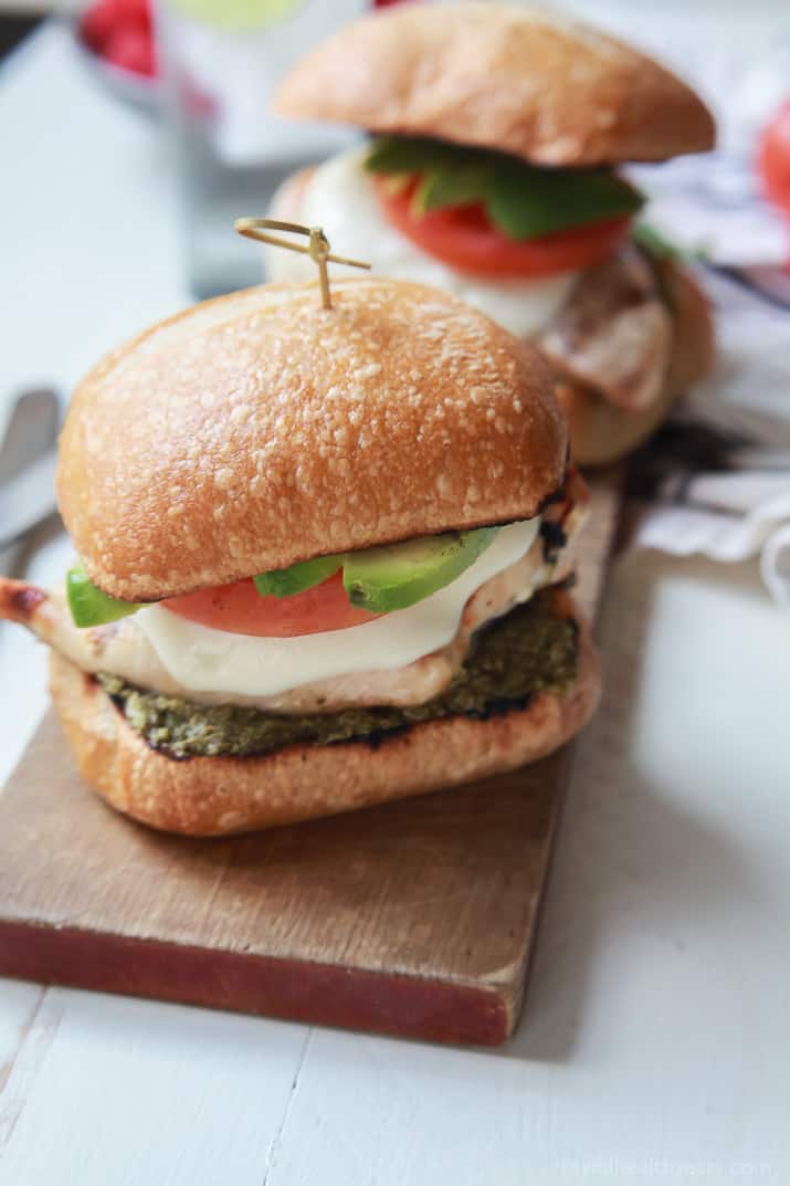 Two Grilled Avocado Caprese Chicken Sandwiches on a wooden board