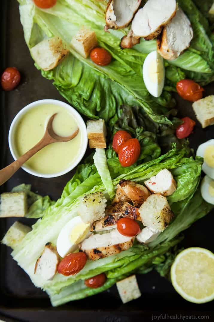 Top view of Grilled Chicken Caesar Salad on whole romaine leaves with a bowl of Caesar dressing
