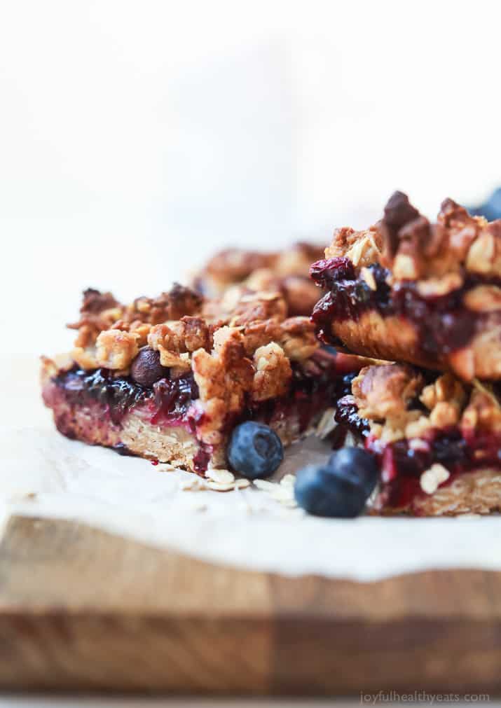 Homemade lemon blueberry bars stacked on top of each other on top of a cutting board.