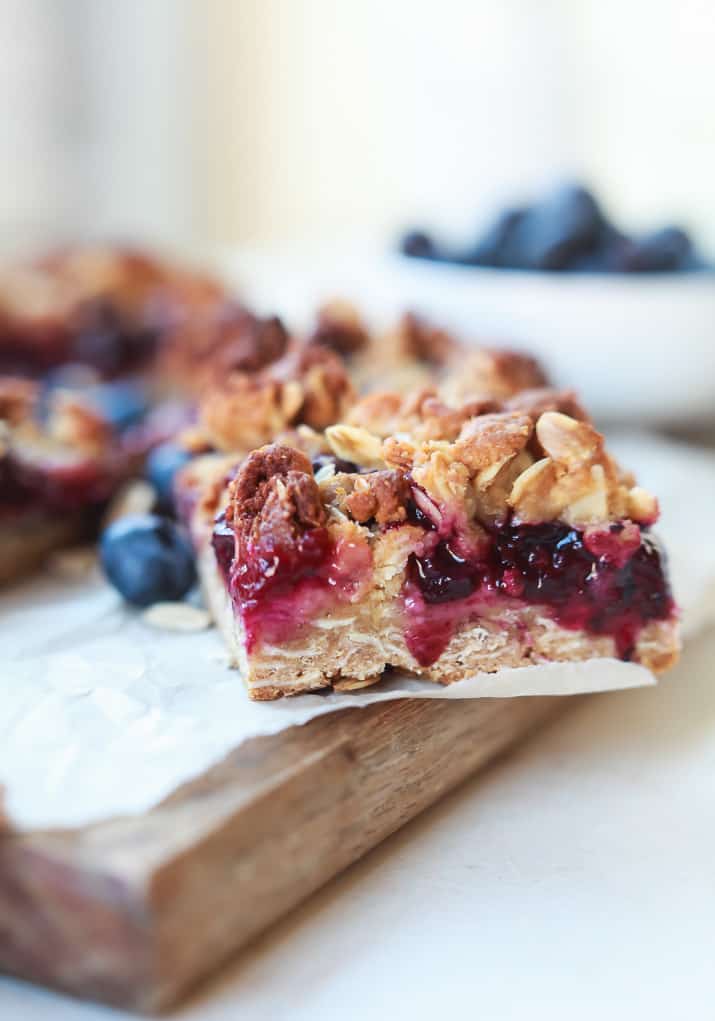 A close-up shot of a blueberry oatmeal breakfast bar on a wooden cutting board