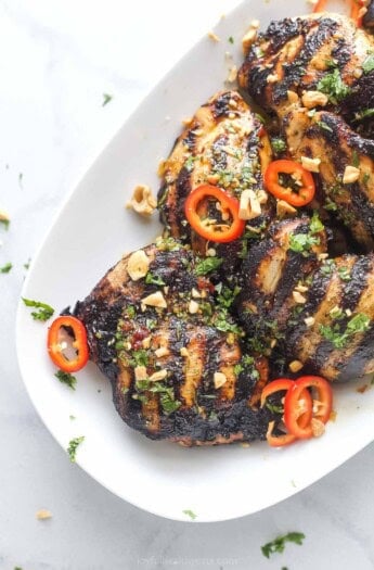 Angled photo of grilled Thai chicken with spicy chilis and chopped cashews.