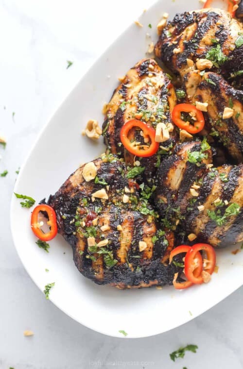 Angled photo of grilled Thai chicken with spicy chilis and chopped cashews.