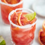 a blood orange margarita with orange wedge and lime wedge garnish