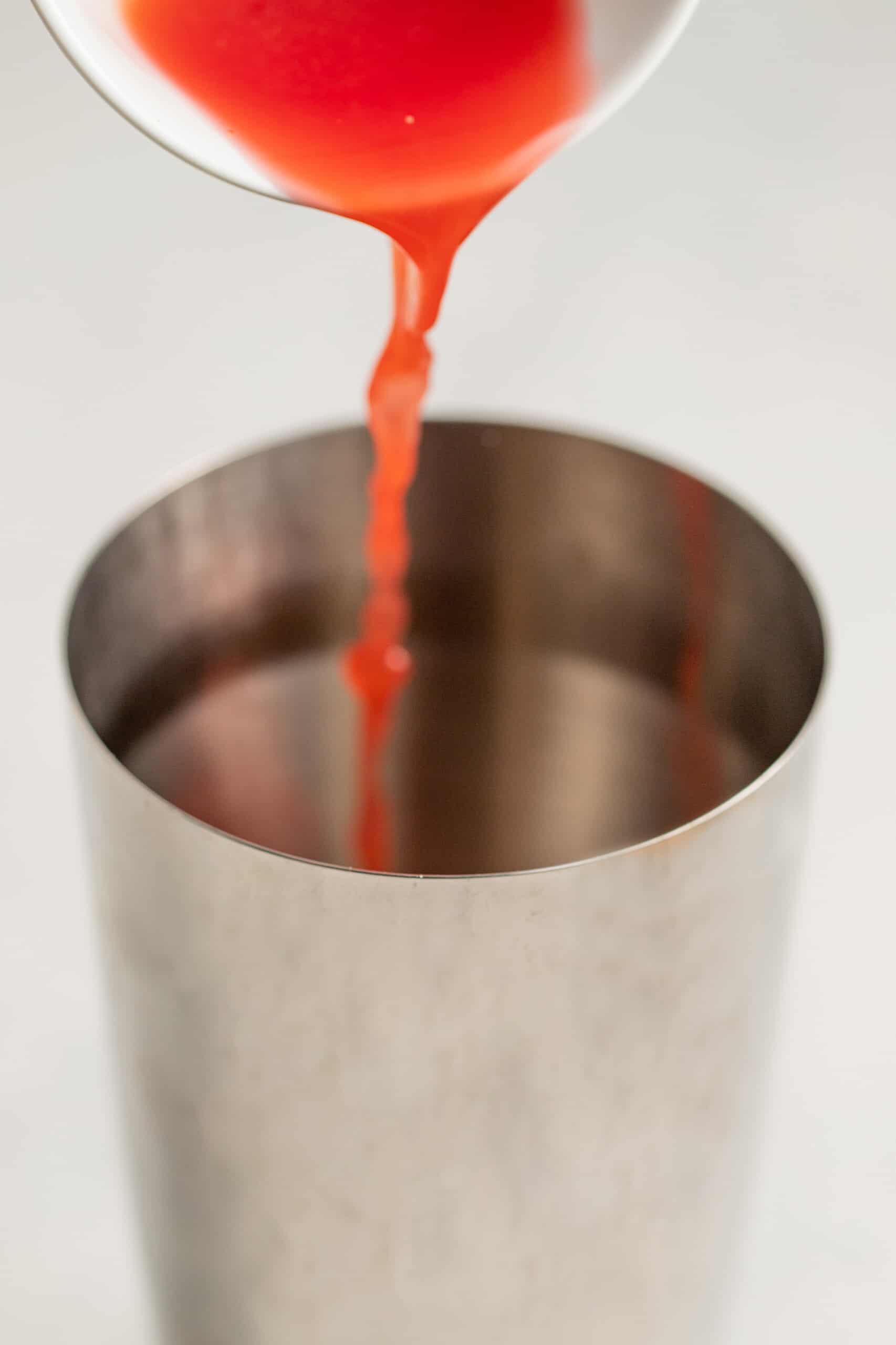 pouring blood orange juice into a cocktail shaker