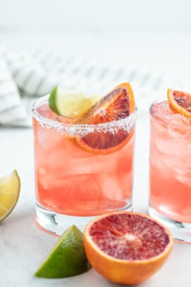 a blood orange margarita with orange wedge and lime wedge garnish