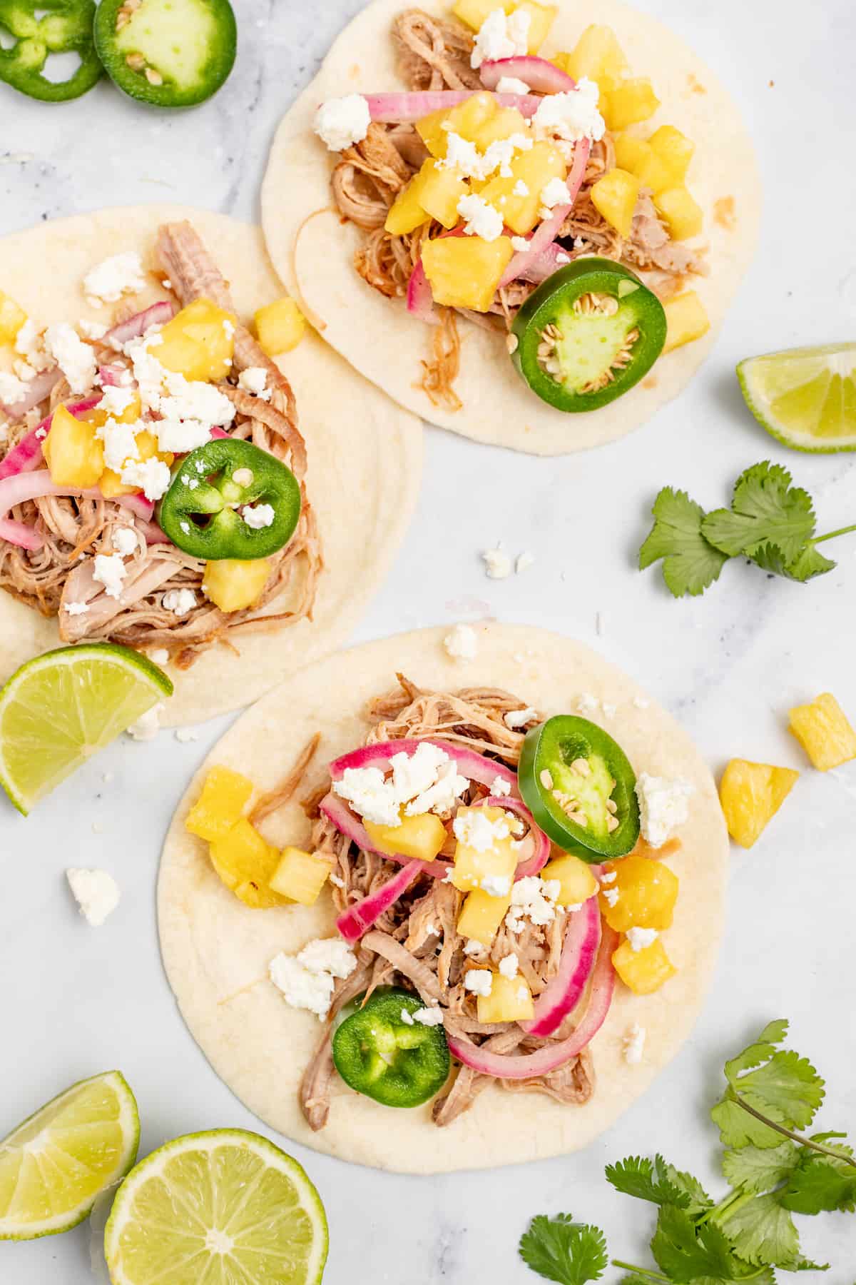 Overhead shot of three pork carnitas tacos with avocado crema and toppings. 