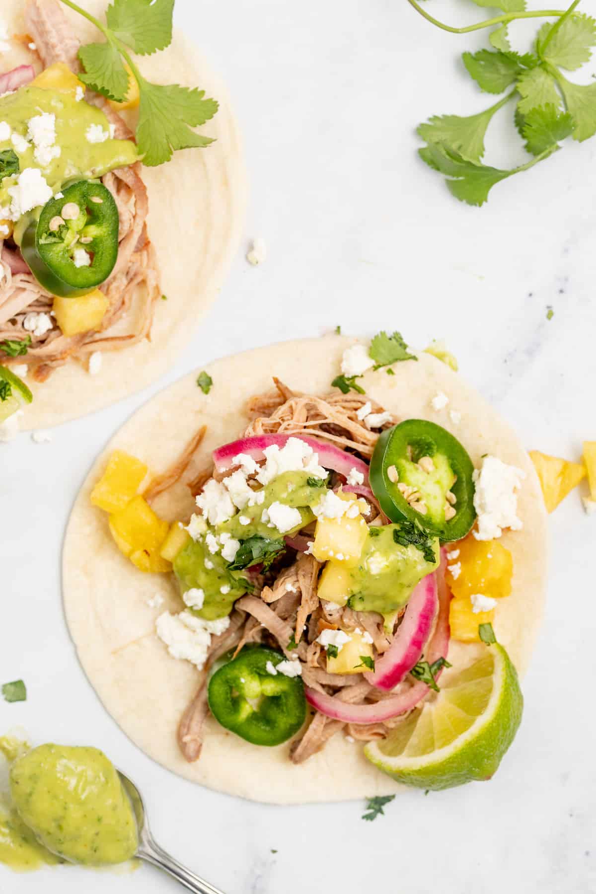 Overhead of carnitas tacos with avocado crema and toppings.