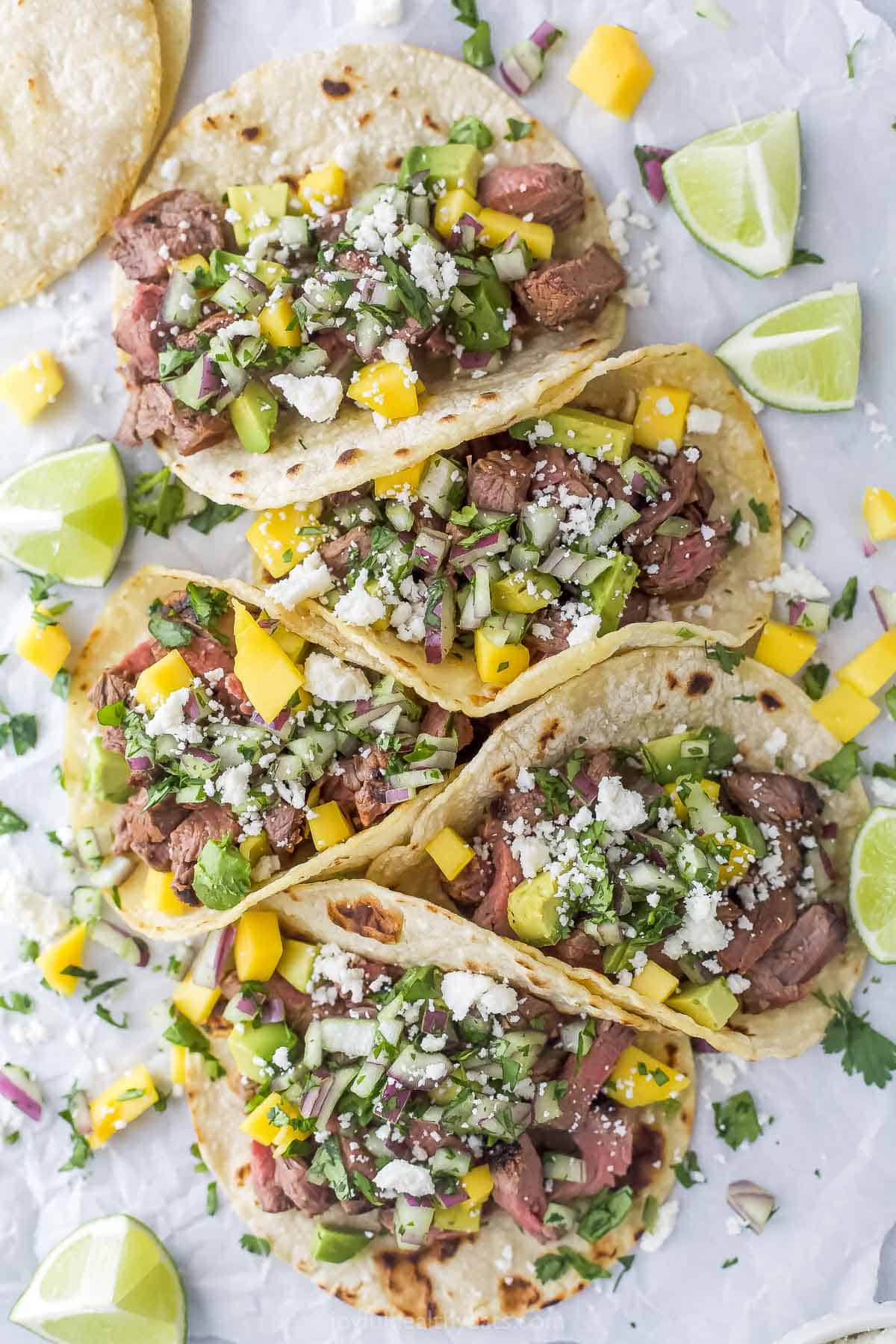 Tacos with toppings and lime wedges on top of parchment paper. 