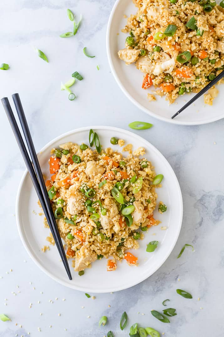 two plates with cauliflower fried rice and chicken with chopsticks