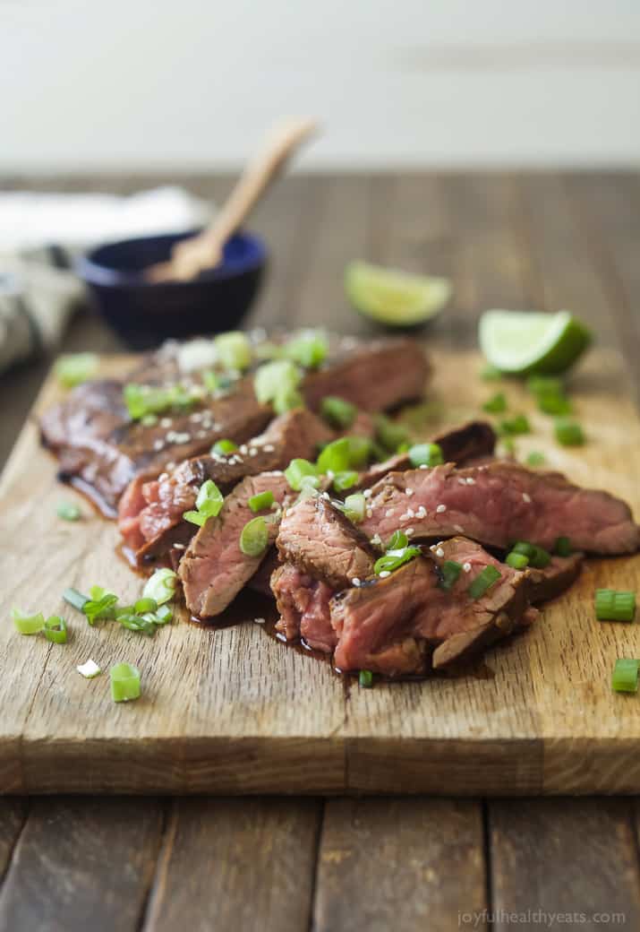 Sliced Asian Grilled Flank Steak on a cutting board with scallions