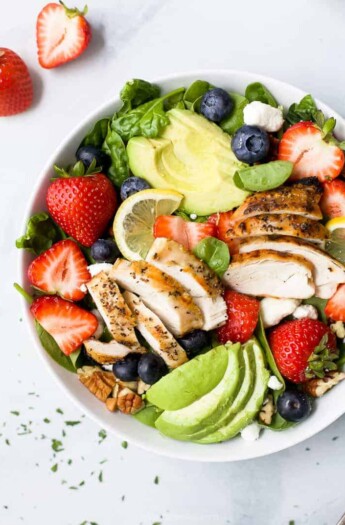 a bowl filled with best avocado strawberry salad with grilled chicken