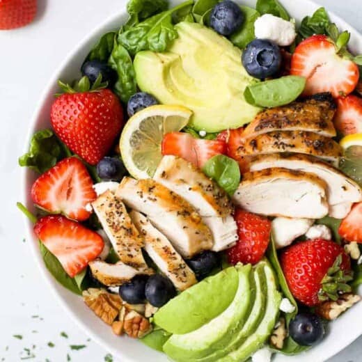 a bowl filled with best avocado strawberry salad with grilled chicken