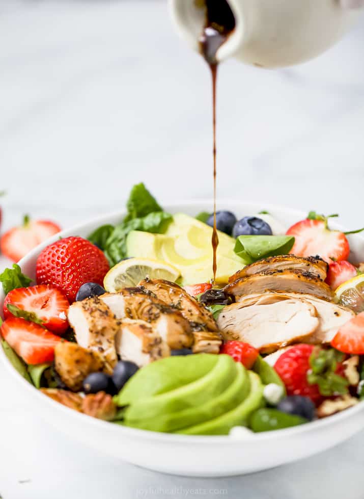 balsamic dressing being poured on best avocado strawberry spinach salad