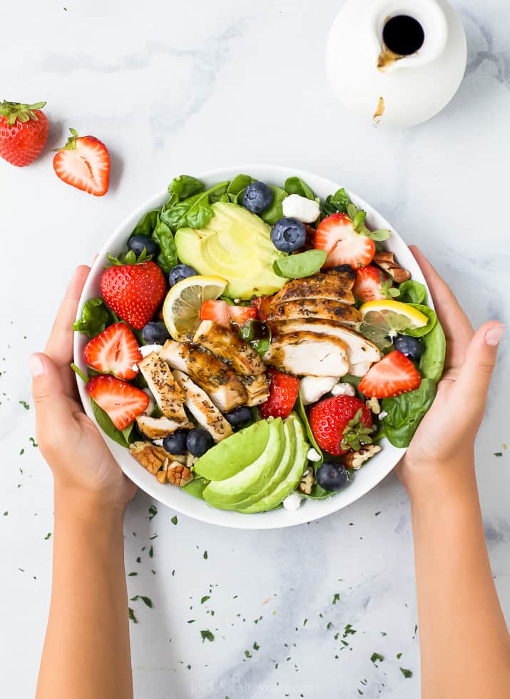 hands holding a bowl filled with the best avocado strawberry salad with grilled chicken