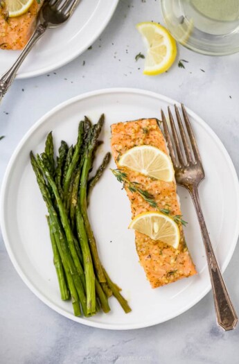 a plate with salmon topped lemon slices and thyme next to asparagus