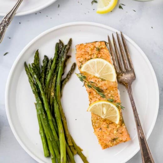 a plate with salmon topped lemon slices and thyme next to asparagus