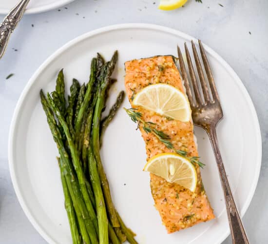 a plate with salmon topped lemon slices and thyme next to asparagus