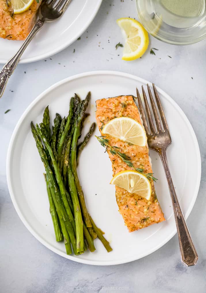 a plate with salmon topped lemon slices and thyme next to asparagus