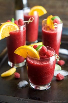 Glasses full of Frozen Raspberry Peach Sangria Recipe served with orange wedges and raspberries