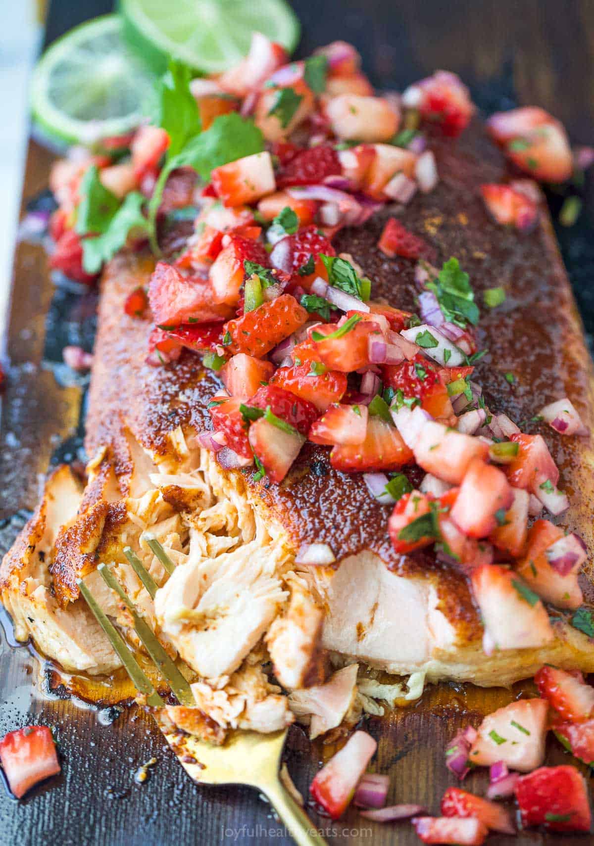 This 25-minute cedar plank salmon with strawberry salsa is flaky, spiced, smokey, and fruity all in one bite. It's perfect for the summer! Flaked salmon with salsa on top.
