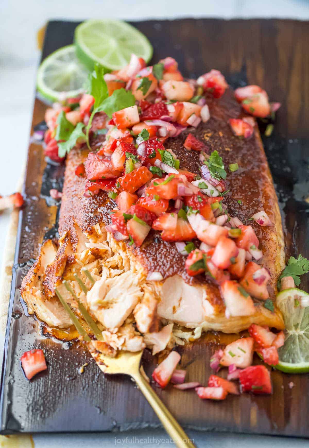 This 25-minute cedar plank salmon with strawberry salsa is flaky, spiced, smokey, and fruity all in one bite. It's perfect for the summer! Flaky grilled salmon on a cedar plank.