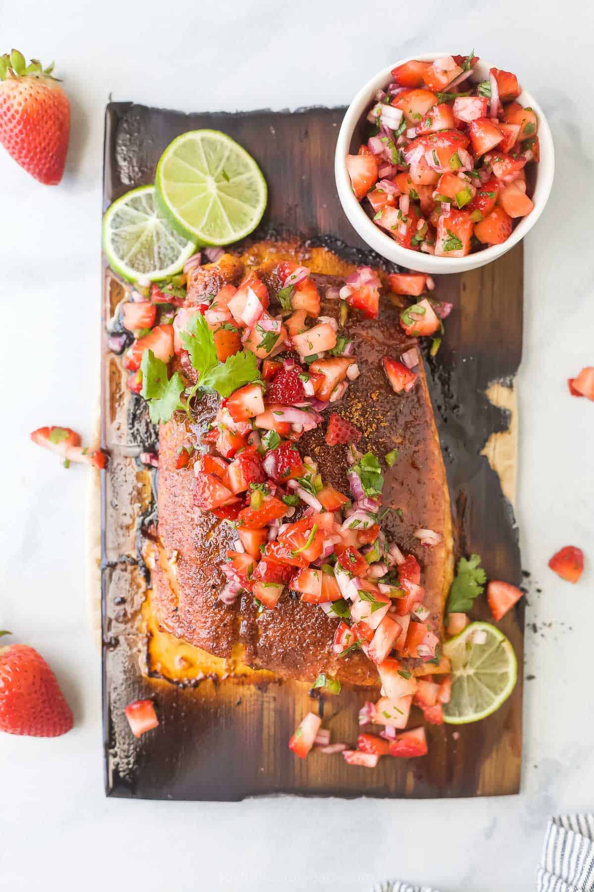 This 25-minute cedar plank salmon with strawberry salsa is flaky, spiced, smokey, and fruity all in one bite. It's perfect for the summer! Overhead shot of cedar plank salmon with strawberry salsa.