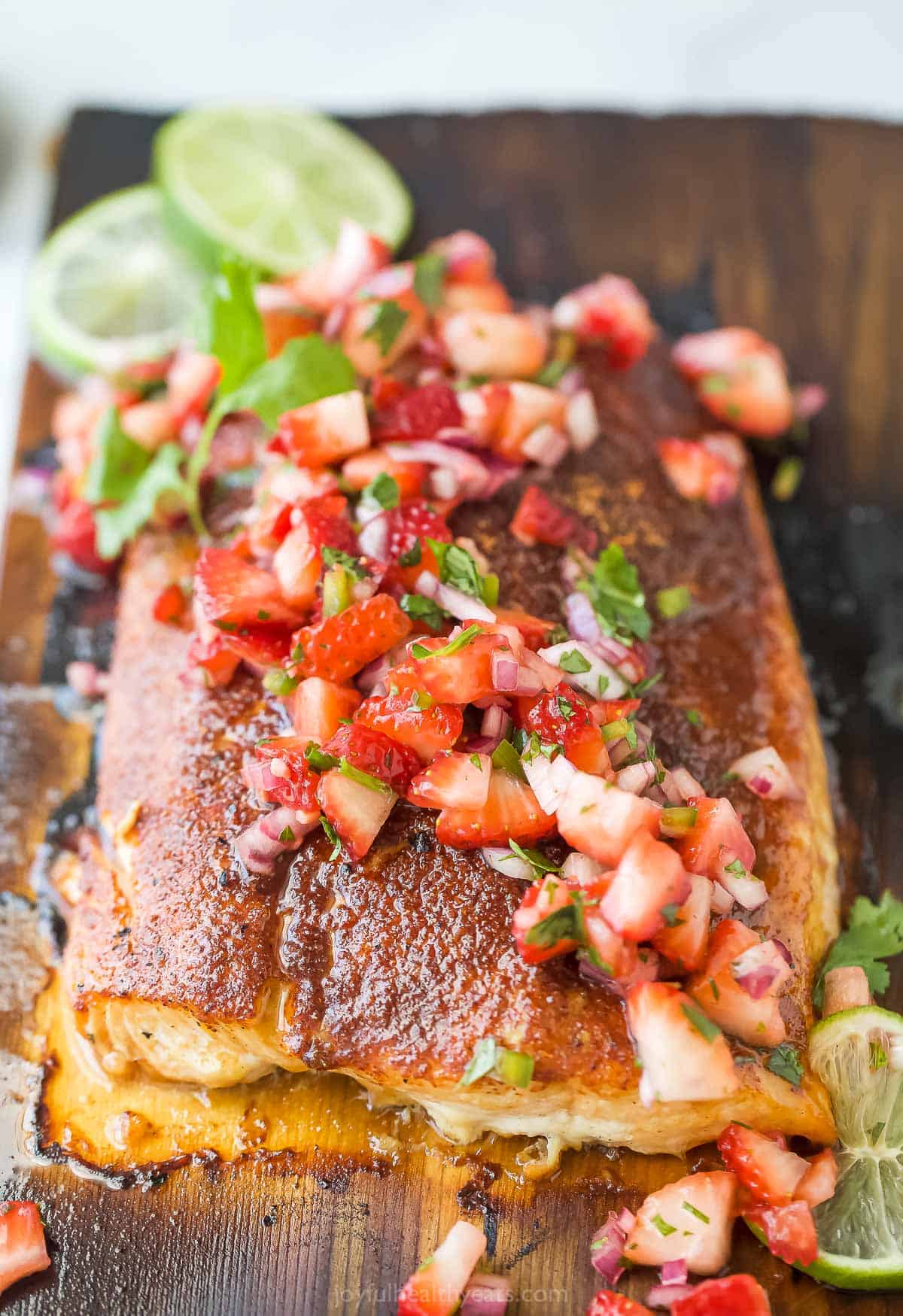 This 25-minute cedar plank salmon with strawberry salsa is flaky, spiced, smokey, and fruity all in one bite. It's perfect for the summer! Close-up of cedar plank salmon with fruity salsa on top.