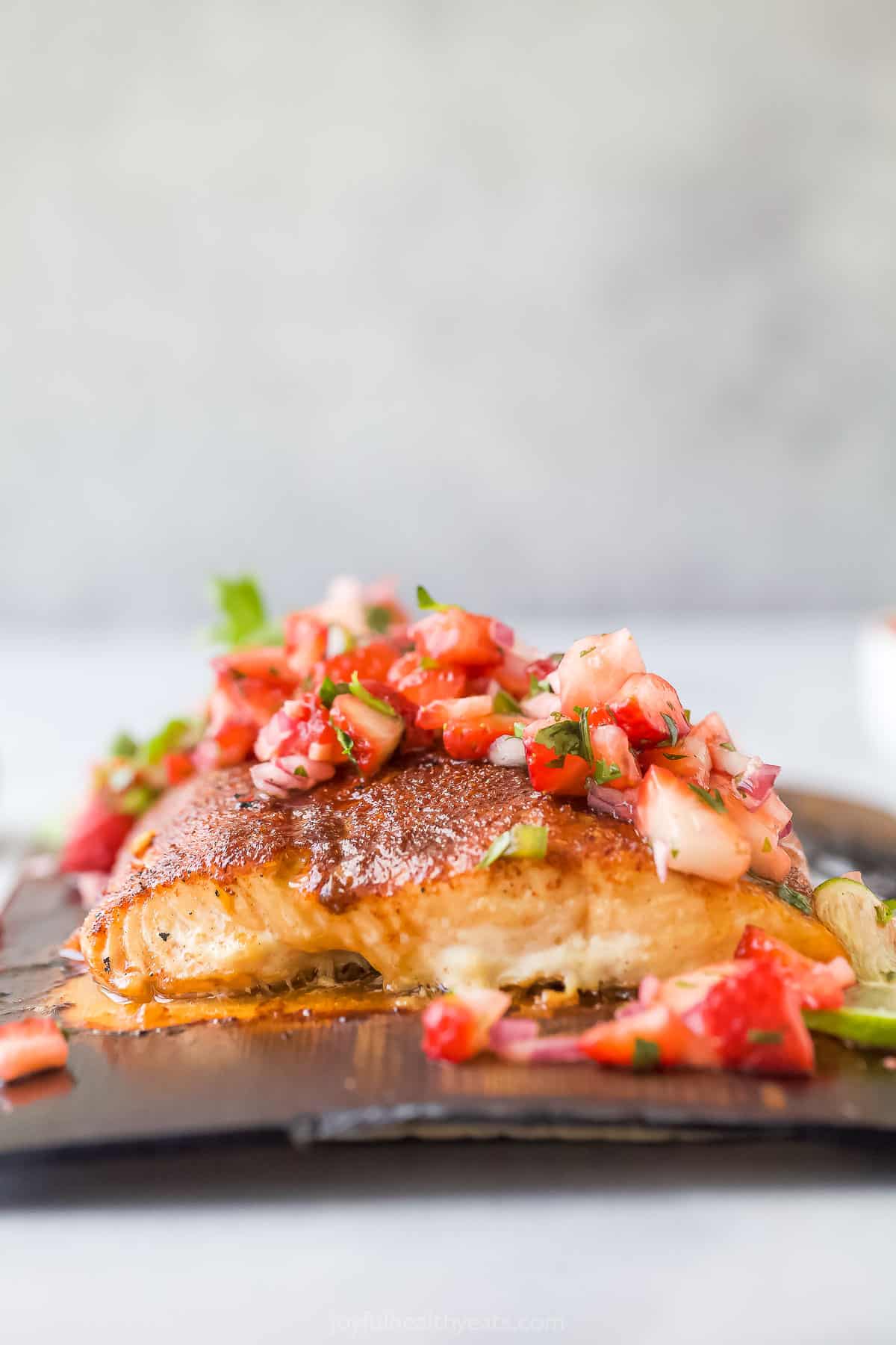 This 25-minute cedar plank salmon with strawberry salsa is flaky, spiced, smokey, and fruity all in one bite. It's perfect for the summer! Side shot of grilled salmon with fruit salsa on top.