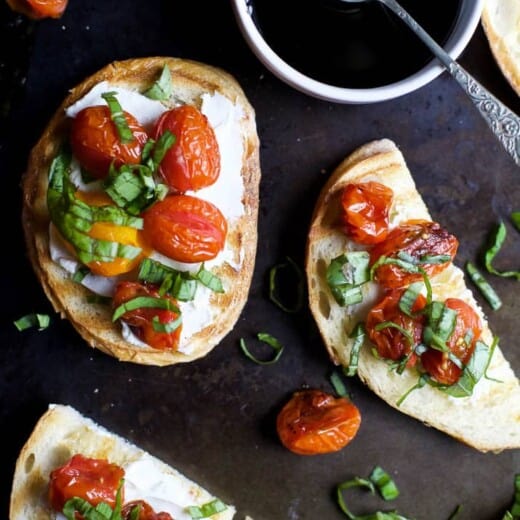 A table with pieces of Roasted Tomato Bruschetta with Whipped Goat Cheese and a bowl of balsamic reduction.