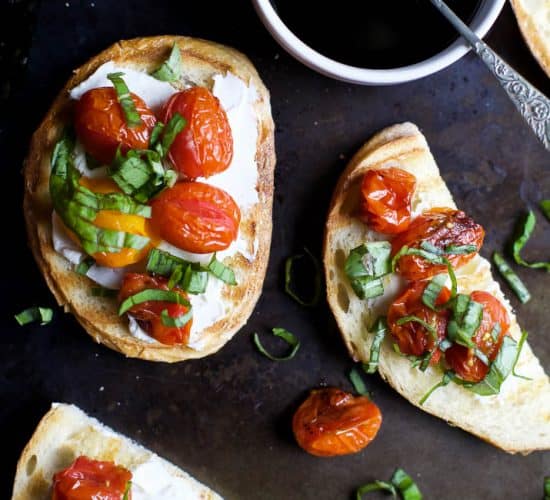 A table with pieces of Roasted Tomato Bruschetta with Whipped Goat Cheese and a bowl of balsamic reduction.