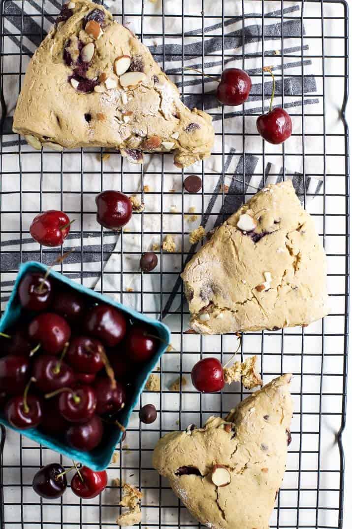 Top view of almond cherry scones and a pint of fresh cherries on a cooling rack