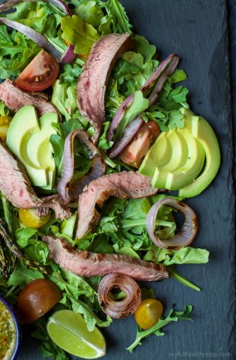A paleo California Steak Salad filled with grilled onions, arugula, avocado, asparagus, charred Steak and covered in zesty Chimichurri Dressing. Fresh, light, high in protein and freakin delicious! You need this! | joyfulhealthyeats.com #glutenfree #paleo
