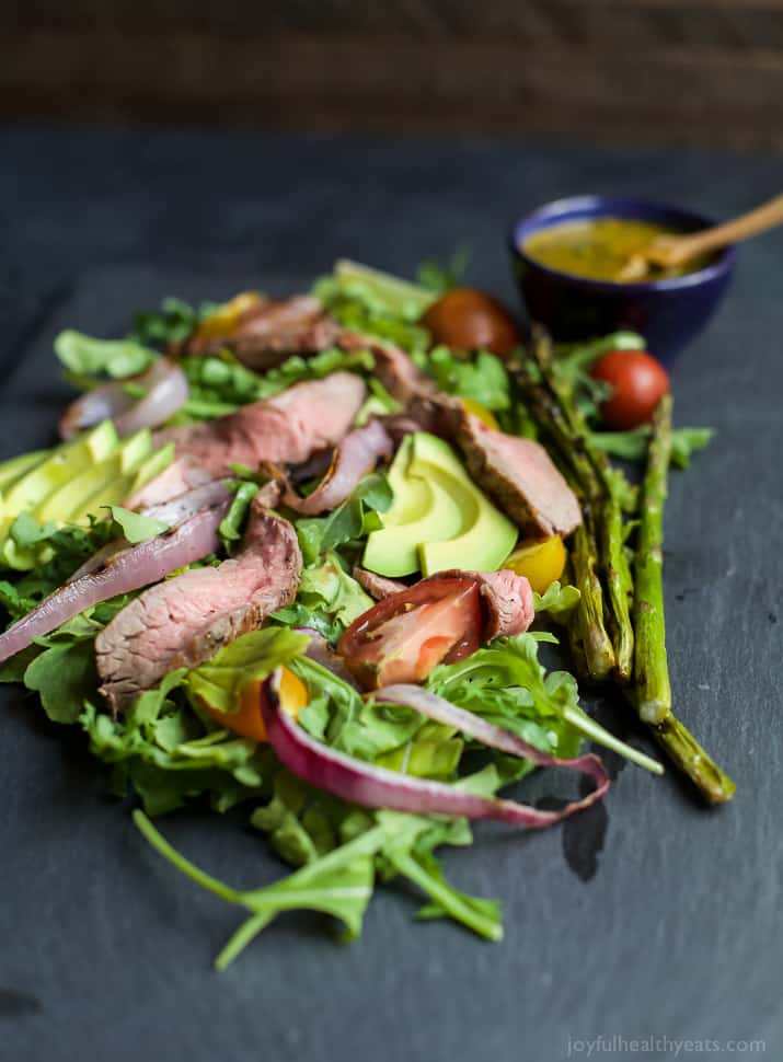 A paleo California Steak Salad filled with grilled onions, arugula, avocado, asparagus, charred Steak and covered in zesty Chimichurri Dressing. Fresh, light, high in protein and freakin delicious! You need this! | joyfulhealthyeats.com #glutenfree #paleo