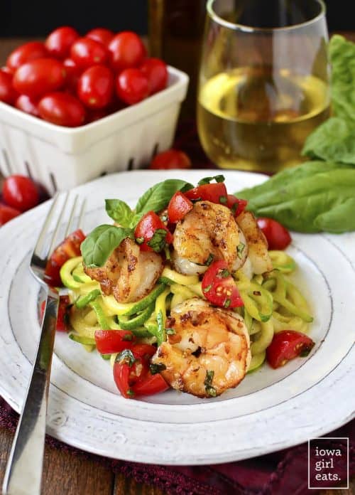 A Plate of Garlicky Tomato Basil Shrimp with Zoodles in Front of a Glass of White Wine