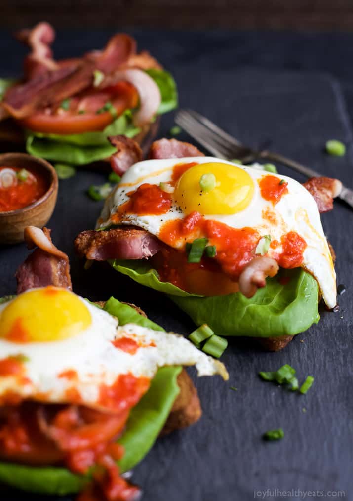 A Couple of Open Faced BLT Sandwiches Topped with Eggs and Spicy Harissa