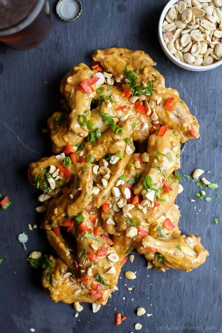 Baked chicken wings coated in Thai peanut sauce with a bowl of peanuts beside them